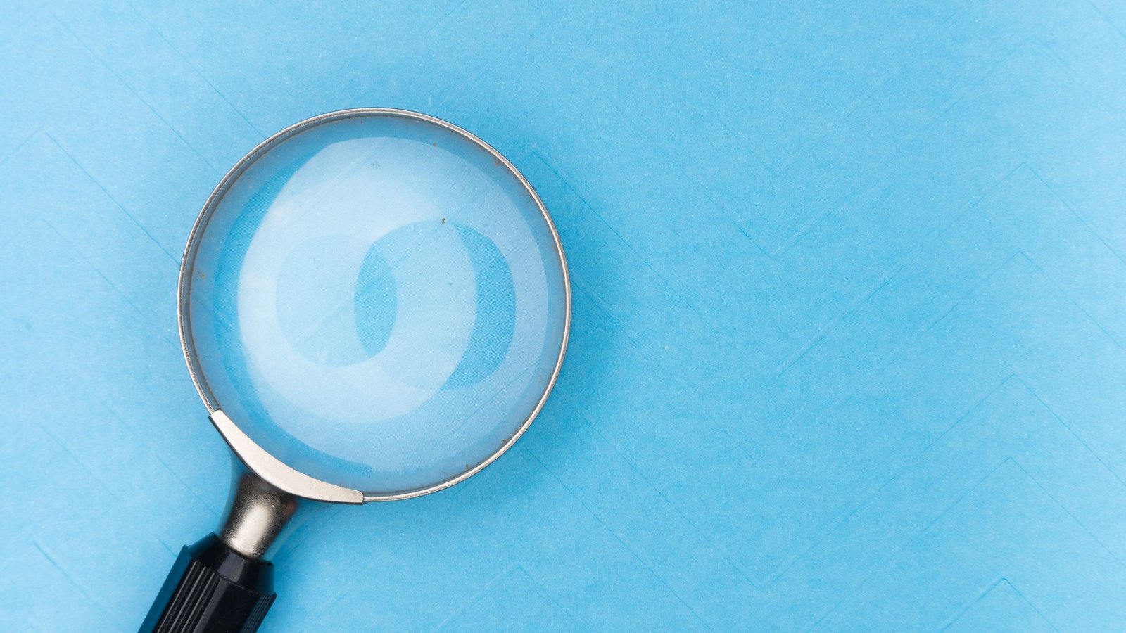 A magnifying glass with a black handle lying on a light blue textured paper surface.