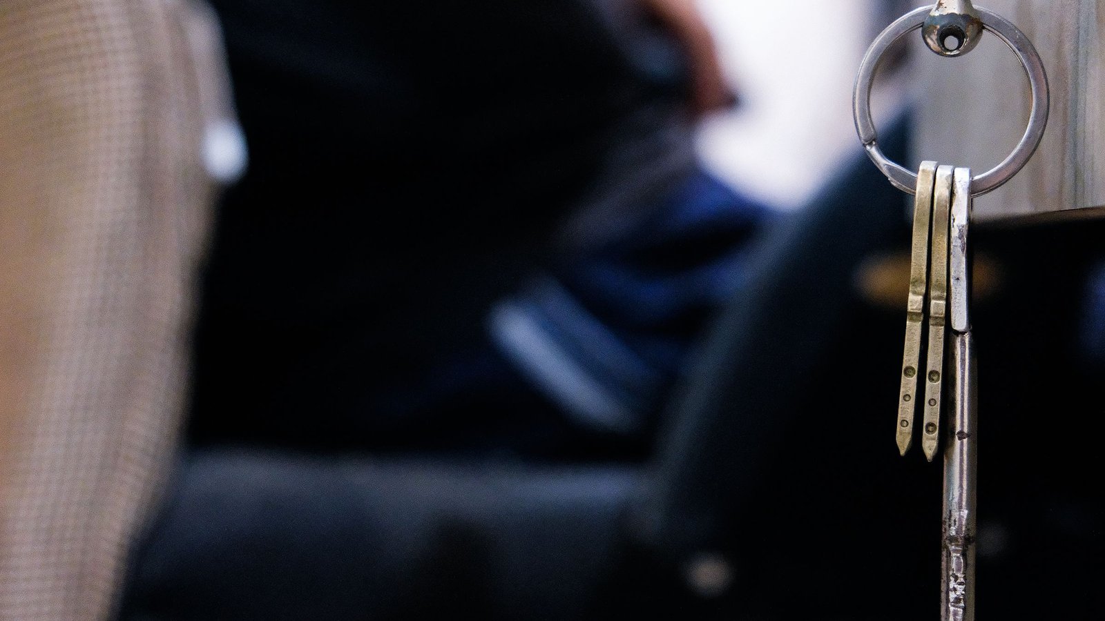A small set of metal keys hanging from a steel key ring on the right, against a dark blue, softly blurred office background.