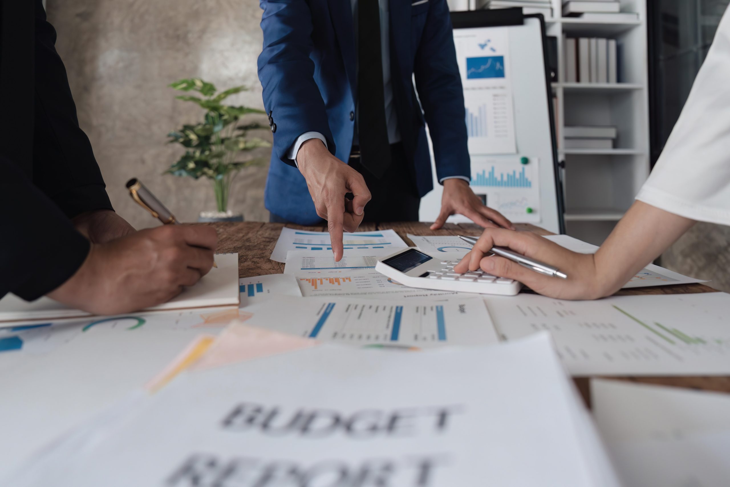 Business team using a calculator to calculate the numbers of statistic business profits growth rate on documents analyzing graph data, desk in the office